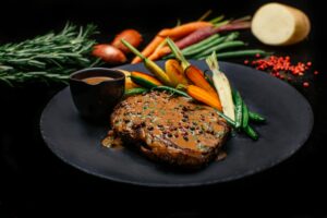 Succulent ribeye steak with peppercorn sauce, served with fresh vegetables on a slate plate.
