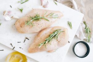 Top-down view of fresh raw chicken breast garnished with rosemary and garlic.