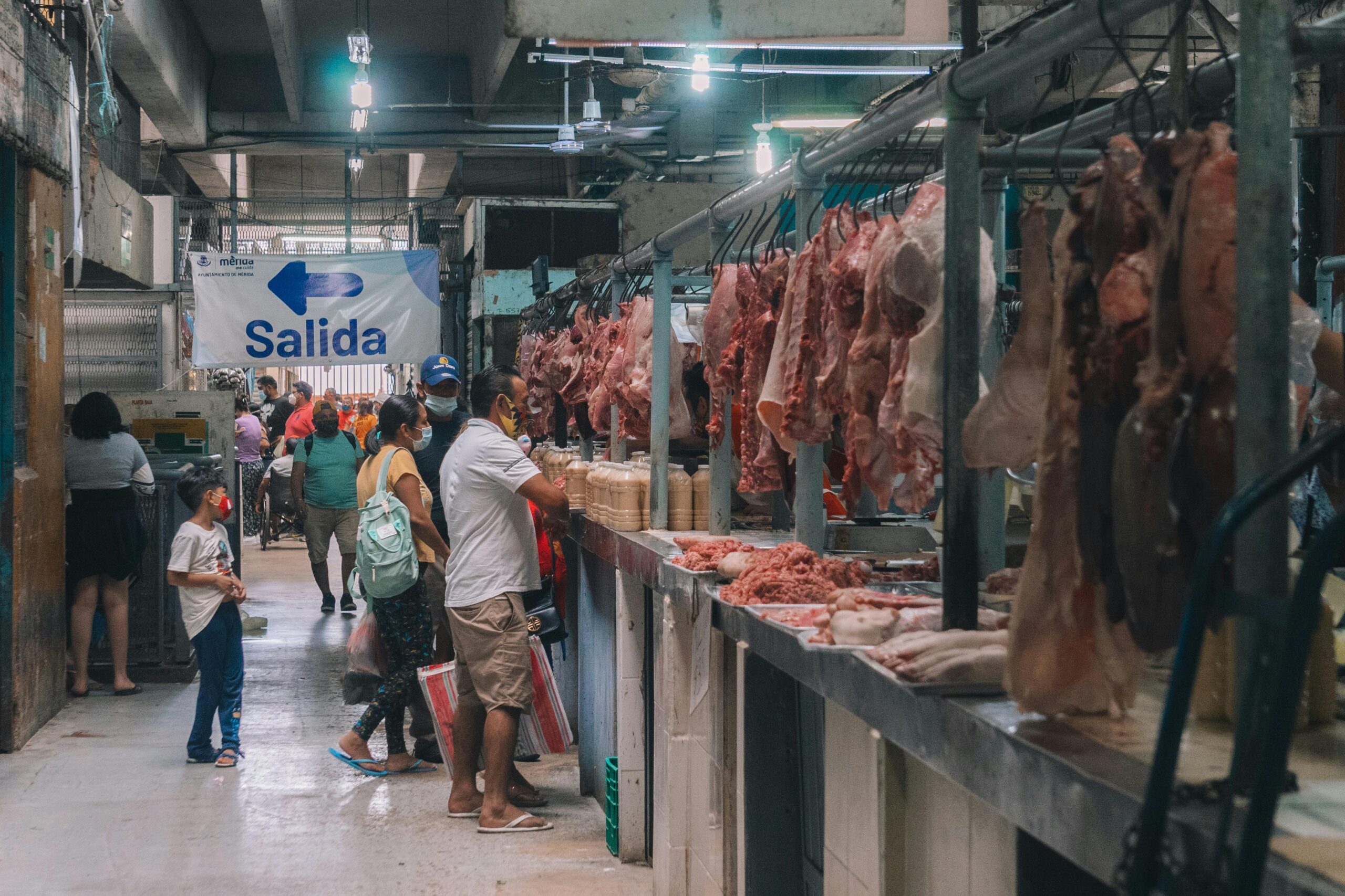 A bustling indoor meat market in Mérida, Yucatán, showcasing various meats and shoppers.